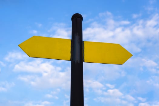 Yellow direction sign on the pole against the blue sky. Yellow arrow signal against sky. photo
