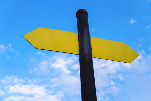 Yellow direction sign on the pole against the blue sky. Yellow arrow signal against sky. photo