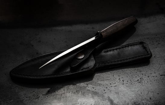 A modern hunting knife and a leather case for him on a dark background. Melee weapons for hunting and self-defense. The instrument of crime. photo