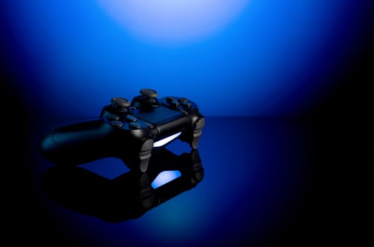 Black gamepad with backlight on blue back. Joystick on glossy surface. photo