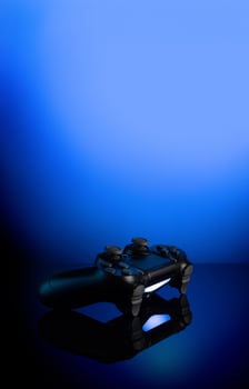 Black gamepad with backlight on blue back. Joystick on glossy surface. photo