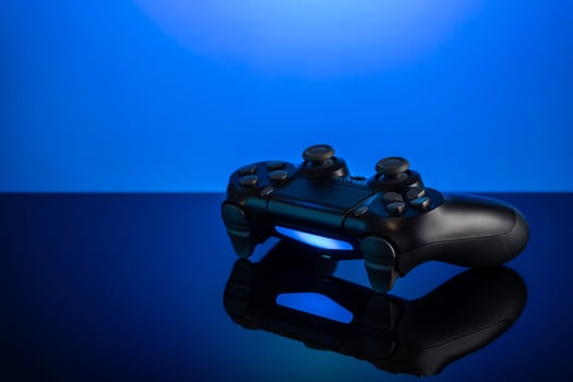 Black gamepad with backlight on blue back. Joystick on glossy surface. photo