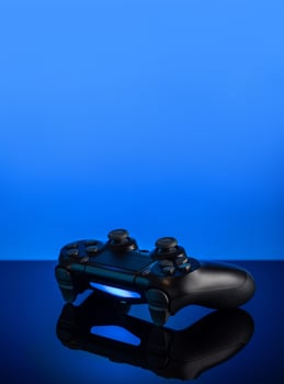 Black gamepad with backlight on blue back. Joystick on glossy surface. photo