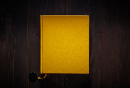 Closed book on vintage wooden back. Yellow book on the wooden table. Closed book with empty cover laying on wooden table. photo