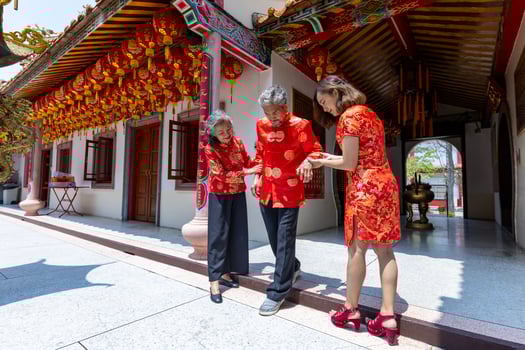 Asian family with senior parent in red cheongsam qipao dress is helping the grandfather to walk into the temple to pay homage to ancestor during Chinese lunar new year in their hometown photo