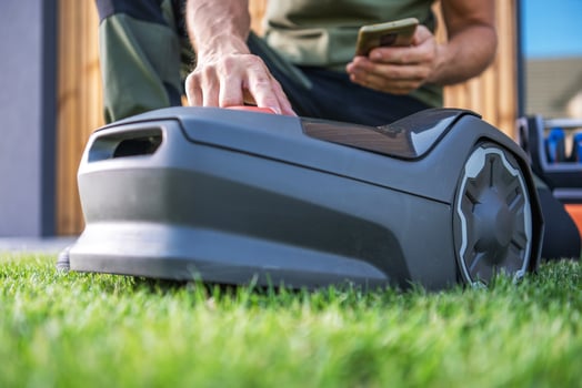 Person Controlling a Robotic Lawn Mower Using a Smartphone on a Sunny Day in the Backyard photo
