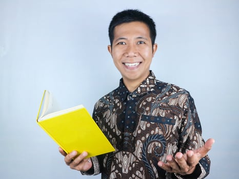 Adult Asian man wearing batik clothes smiling while holding a book photo