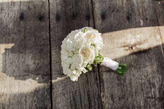 A bouquet of white flowers sits on a wooden table. The flowers are arranged in a vase and are the main focus of the image. The wooden table provides a rustic and natural backdrop for the flowers photo