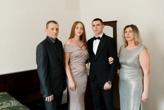 A man and woman in black suits are standing next to a man and woman in silver dresses. The family is posing for a picture photo