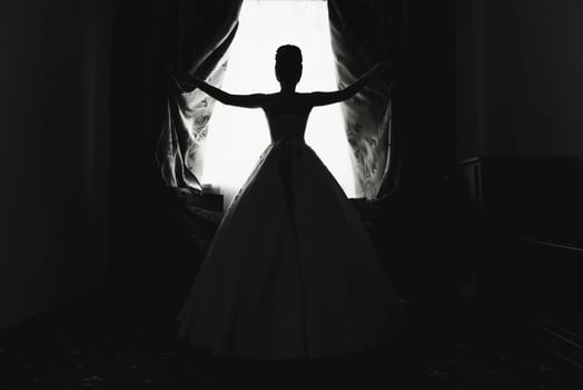 A woman in a wedding dress is standing in front of a window. Scene is elegant and romantic photo