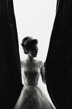 A woman in a wedding dress is standing in front of a curtain. She is wearing a tiara and has her hair in a bun. The image has a romantic and elegant mood photo