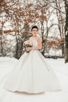 A woman in a white dress is standing in the snow with a bouquet of flowers in her hand photo