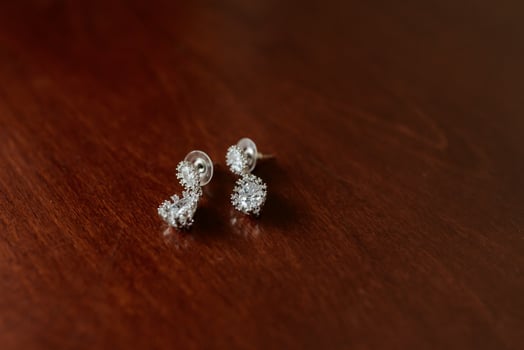 Two earrings with diamonds on them are sitting on a wooden table photo