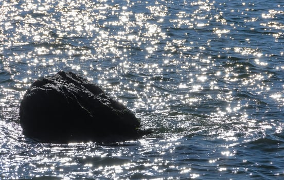Bright reflections on the water on a sunny day among the coastal rocks near the Black Sea coast photo
