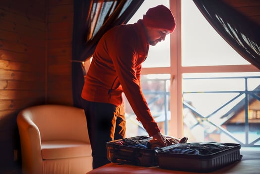 Stylish hipster traveller man in red hat in wooden house packing suitcase photo