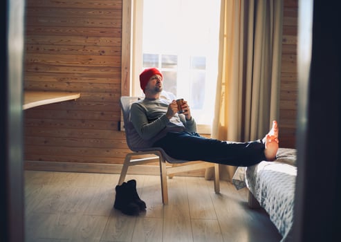 Winter male traveller in red hat holds wooden mug of mulled wine or hot tea with by the window photo