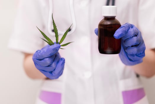 A medic professional in a lab coat and blue gloves holds a cannabis leaf and a mockup of a glass dark bottle of medicine. Hemp medicinal properties concept. photo