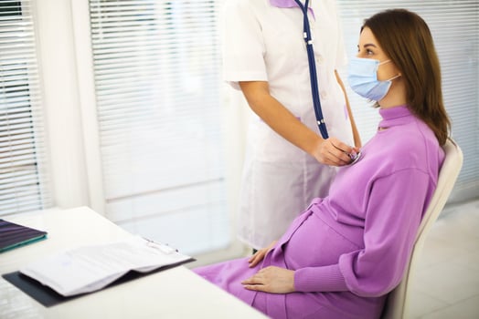 Doctor listening to pregnant woman heartbeat with stethoscope during prenatal care appointment in hospita photo