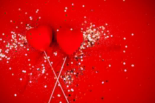 Two decorative hearts on a stick with ribbon. Bright background with silver sequins and round confetti. photo