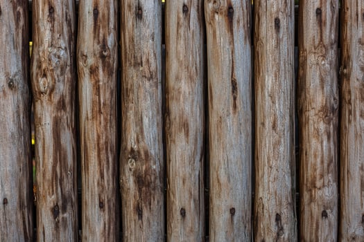 A fence made of roughly processed boards. A palisade of rough logs. Wood back photo