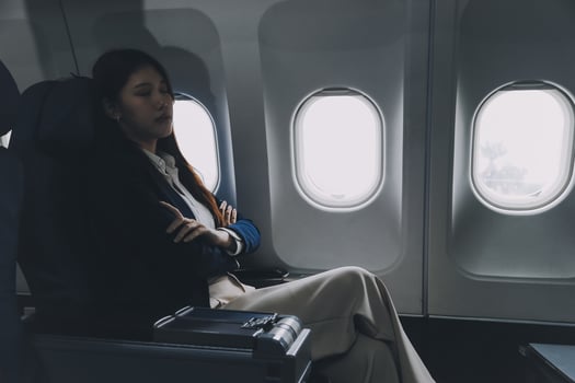 Photo of a frustrated woman sitting on an airplane with her head in her hands. Asian woman sitting in a seat in airplane