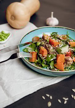 Salad of fresh vegetables, baked pumpkin, quinoa, decorated with sunflower seeds and green beans on a turquoise plate, served with fork, knife, cutlery. Black, white background, isolated, vertical photo