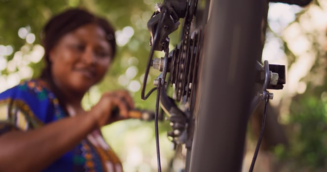 Dedicated sporty african american woman checking performance of bicycle parts by spinning the pedals. Active female cyclist ensuring proper function of tire close-up of bike wheel in home yard. photo