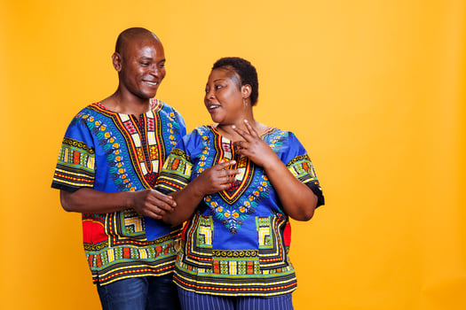 Smiling man and woman romantic pair chatting while standing in studio. Happy wife and husband wearing ethnic african american clothes talking and posing on orange background photo