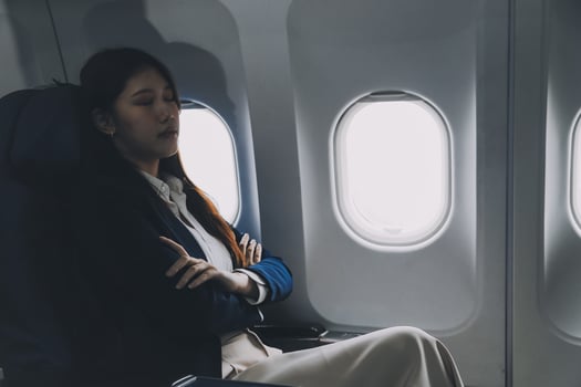 Photo of a frustrated woman sitting on an airplane with her head in her hands. Asian woman sitting in a seat in airplane