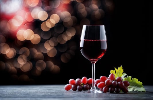 Glass of red wine and handful of ripe grapes on wooden surface with dark background photo