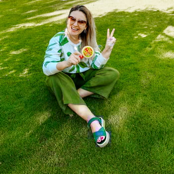 Happy young woman blowing bubbles with bubble machine and laughing while sitting on green grass photo