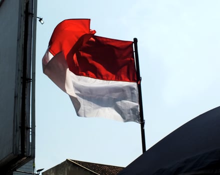Indonesia national flag waving in the wind between city building and public facility with clear blue sky background. Nation patriotism. The Hari Kemerdekaan Indonesia photo