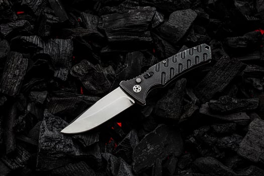 Folding knife on charcoal with red streaks of heat. Dark back. photo