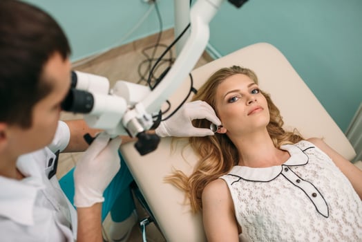A clinician examines a patient's ear with a microscope in a medical office photo