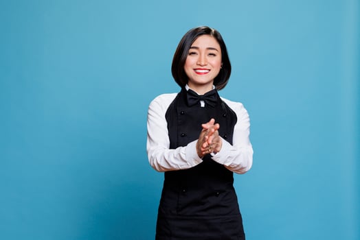 Smiling asian waitress wearing uniform applauding with to show support and appreciation portrait. Cheerful young attractive woman receptionist clapping hands and looking at camera photo