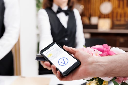 Close-up shot of caucasian old man making payment transaction using mobile phone at registration counter. Detailed view of a person using smartphone to pay for check-in reservation at hotel reception. photo