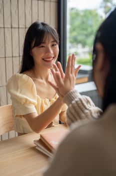 A beautiful Asian woman is giving a high five to her friend while sitting together in a room. photo