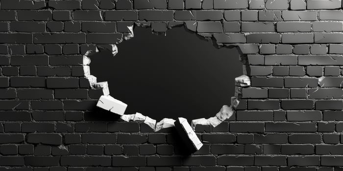 The image shows a damaged wall with a large hole and cracked edges, contrasting with surrounding black bricks, evoking a sense of depth, decay, and inviting thoughts on time and neglect photo