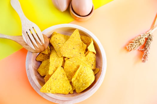 Corn chips on wooden plate isolated on orange and yellow background. Crispy snack dessert. Food Photography Concept photo