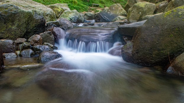 A picturesque cascade flowing gently over mossy rocks, nestled among towering trees. photo