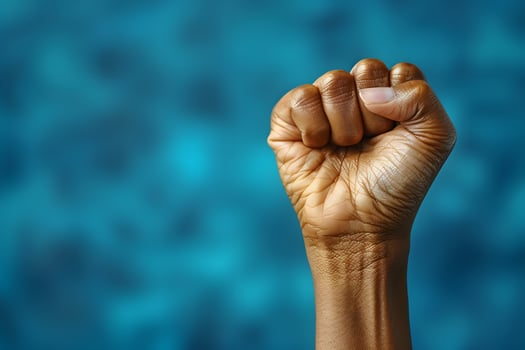 Power and Strength - Close-Up of a Raised Fist in Front of Blurred Blue Background - Symbol of Unity and Resilience photo