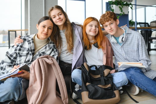 A group of cheerful student friends are sitting on the floor in a classroom photo