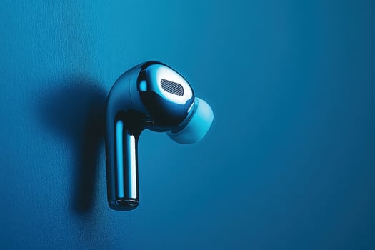 A stylish wireless earbud floats effortlessly, reflecting light in a captivating blue setting, embodying modern design and technology. photo