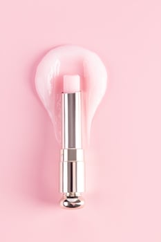 An open package of a tube of lip balm with a delicate structure to moisturize and nourish the lips lies on a sample of rose balm. vertical top view photo