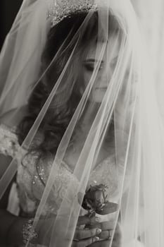 A woman is wearing a veil and holding a rose. The veil is white and covers her face, creating a sense of mystery and elegance. The rose adds a touch of romance and beauty to the scene photo