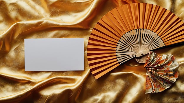 A mockup of a blank business card lying on golden Japanese silk, next to it lies a dancing Japanese fan photo