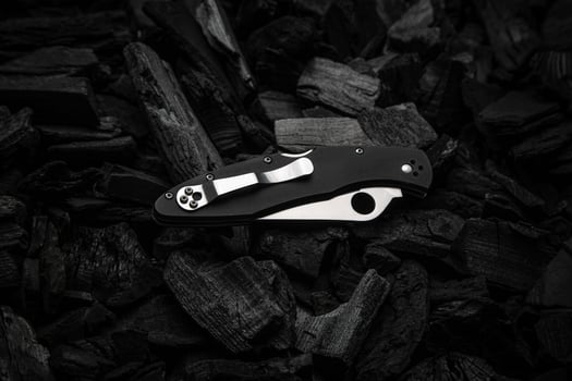 Modern knife with a silver blade. Hunting, military folding knife on smoldering charcoal. Black back. photo
