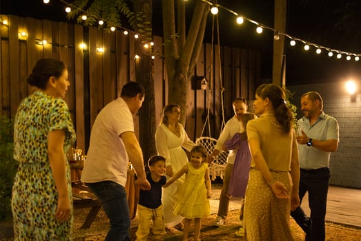 Bride and groom dancing first dance in front of best friends and kids, relatives and guests at illuminated backyard photo