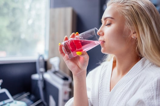 Young blond woman in a white coat with her eyes closed drinks a vitamin cocktail in a beauty salon or clinic. Modern interior. photo