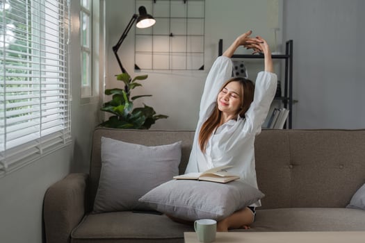 Young Woman Enjoying Her Morning Routine with Stretching and Relaxation on a Cozy Sofa in a Modern Living Room photo